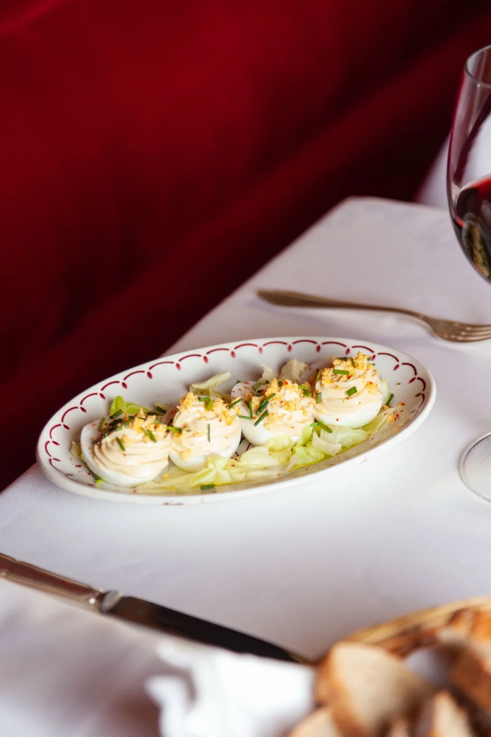 Assiette d'œufs mimosa du Café Max sur nappe blanche, jaune râpé et ciboulette sur la mayonnaise, devant la banquette de velours rouge