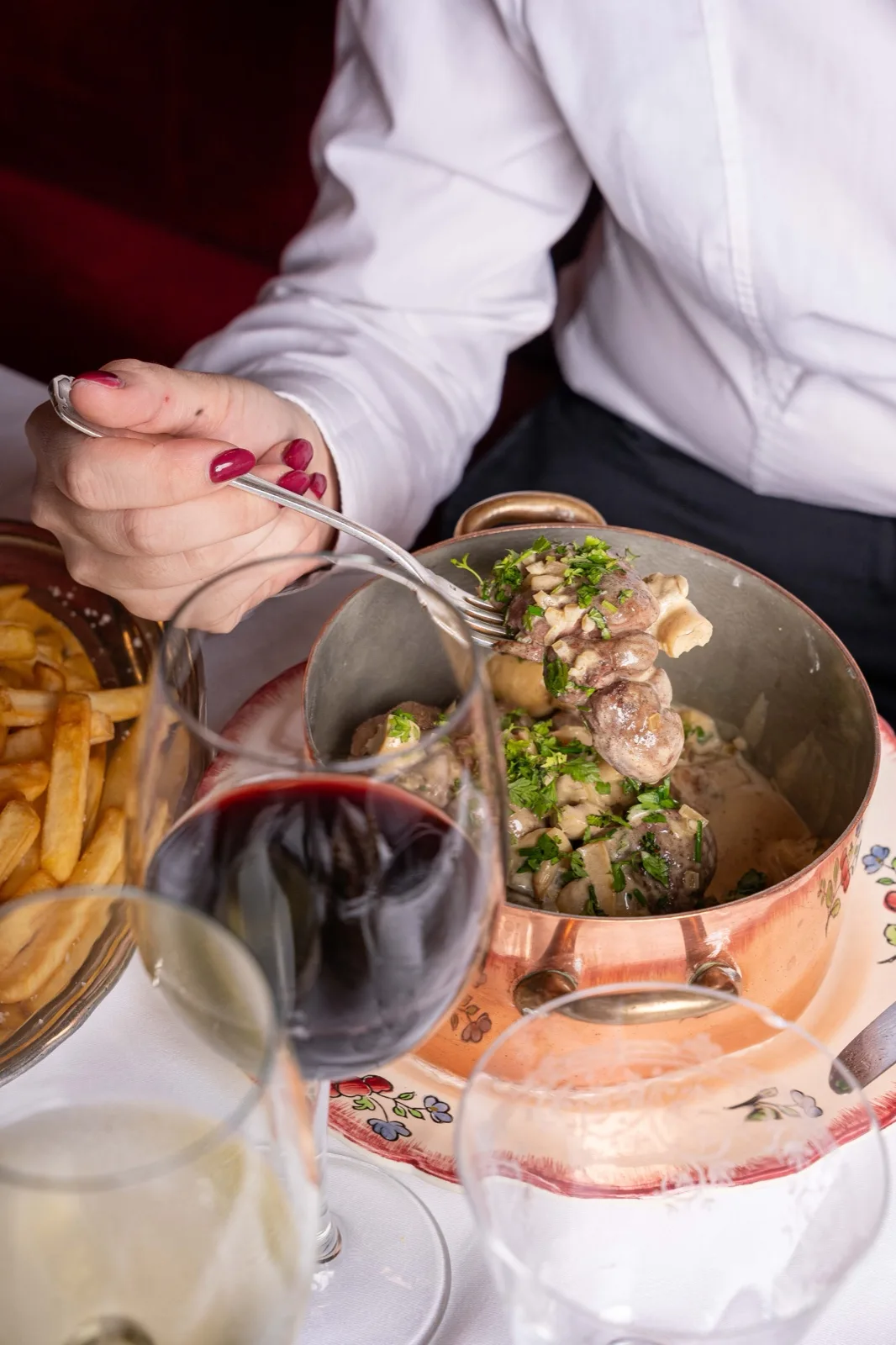 Cocotte de cuivre du Café Max servie à table avec des frites maison, un verre de rouge et la banquette de velours en arrière-plan