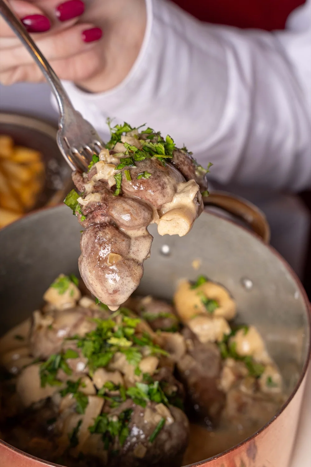 Bouchée de rognon de veau nappée de sauce à la crème, champignons de Paris et échalote ciselée, soulevée à la fourchette au-dessus de la cocotte de cuivre